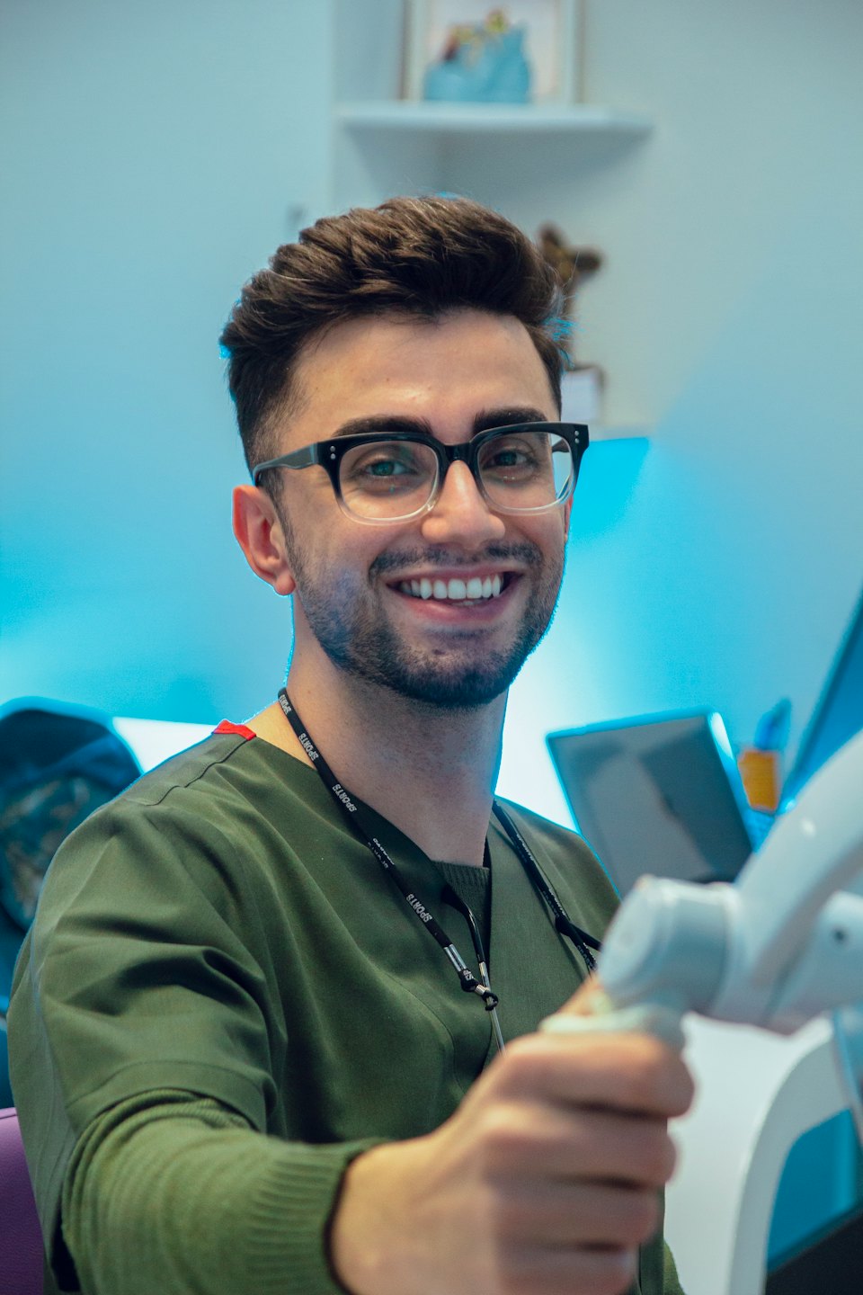 A young man in scrubs holds a medical device in a clinic.