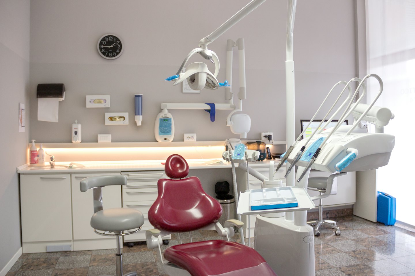 Modern dentist's office with red chair and medical instruments.